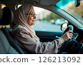 An elderly Muslim woman in gray hijab and glasses driving car 126213092