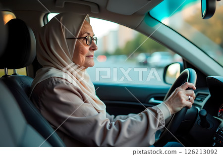 An elderly Muslim woman in gray hijab and glasses driving car 126213092