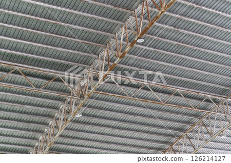 Industrial ceiling with exposed beams and structural elements in modern building, showing metal trusses and corrugated panels with weathered look Industrial ceiling with exposed beams and structural elements in modern building, showing metal trusses and corrugated panels with weathered look 126214127