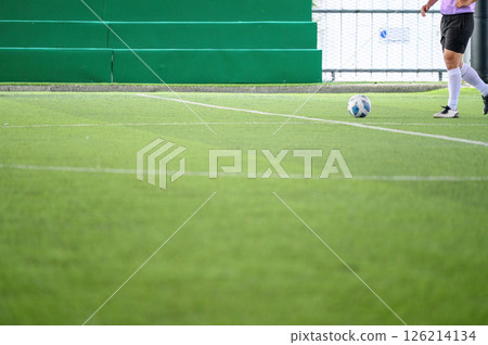Soccer player on green grass field with white lines preparing to kick ball near green bleachers in bright daylight Soccer player on green grass field with white lines preparing to kick ball near green bleachers in bright daylight 126214134