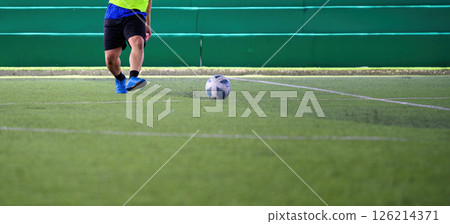 Soccer player kicking ball on green grass field during game with green stadium seats in background showing action and movement Soccer player kicking ball on green grass field during game with green stadium seats in background showing action and movement 126214371