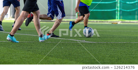 Soccer players in action during game on grass field focusing on their legs and ball, showing dynamic movement and teamwork in lively sports setting 126214376