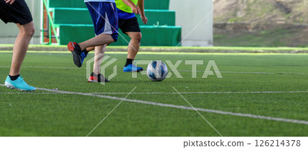 Soccer players in action on green grass field focusing on their legs and ball during game with vibrant energy and movement 126214378