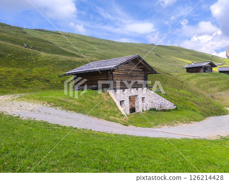 Historic wooden barn nestled in lush green hills showcases tranquil alpine life during a sunny day 126214428