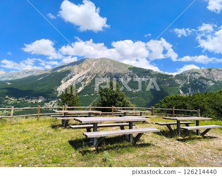 Scenic picnic area with wooden tables surrounded by breathtaking mountains under a clear blue sky 126214440