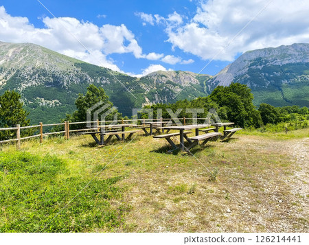 Tranquil picnic area with wooden tables amidst majestic mountains on a sunny day Tranquil picnic area with wooden tables amidst majestic mountains on a sunny day 126214441