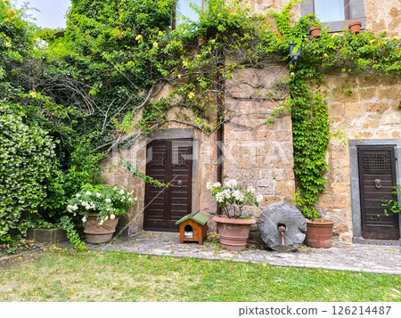 Charming stone cottage garden decorated with lush greenery, blooming flowers, and rustic elements in a serene countryside setting Charming stone cottage garden decorated with lush greenery, blooming flowers, and rustic elements in a serene countryside setting 126214487