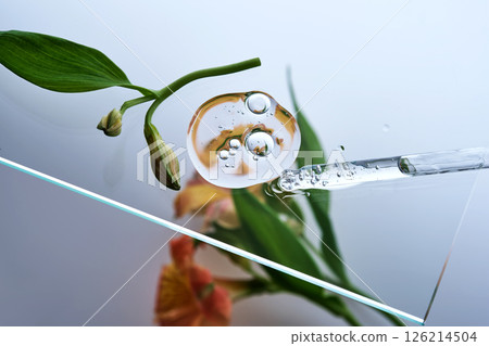 A pipette with a beautiful drop of serum on a background of lily flowers. A pipette with a beautiful drop of serum on a background of lily flowers. 126214504
