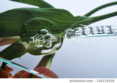 A pipette with a beautiful drop of serum on a background of lily flowers. 126214508