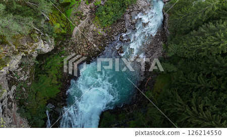Majestic river flows through lush green landscape with rocky banks under bright sunlight 126214550