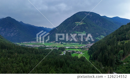 Breathtaking view of green valleys and majestic mountains near a serene village during a cloudy afternoon in the Alps Breathtaking view of green valleys and majestic mountains near a serene village during a cloudy afternoon in the Alps 126214552
