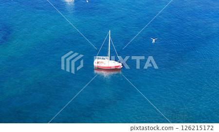 Serene sailboat gliding on crystal-clear water under a bright midday sun near a tranquil bay Serene sailboat gliding on crystal-clear water under a bright midday sun near a tranquil bay 126215172