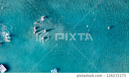 Vibrant summer day with sunbathers and swimmers enjoying crystal-clear water in a peaceful coastal setting 126215173