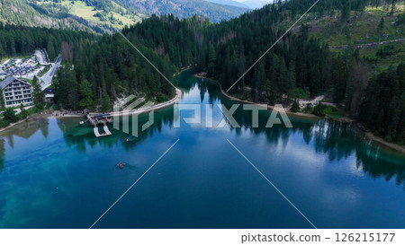 Serene lake surrounded by lush forests and mountains with vibrant reflections during a calm day Serene lake surrounded by lush forests and mountains with vibrant reflections during a calm day 126215177