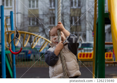 A smiling girl -marsh, rising to a rope on a colorful playground, enjoying classes in the fresh air, developing motor skills and contributing to a feeling of adventure and joy in her childhood. A smiling girl -marsh, rising to a rope on a colorful playground, enjoying classes in the fresh air, developing motor skills and contributing to a feeling of adventure and joy in her childhood. 126215640