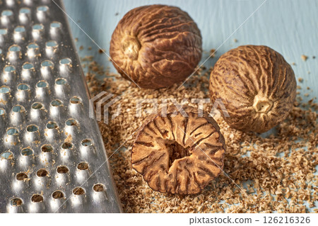 three nutmegs and a metal grater on a blue wooden table 126216326