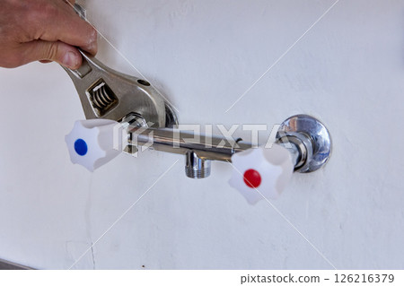 Tightening of wall-mounted tap connection is performed by plumber using adjustable wrench with smooth jaws suitable for gripping flat surfaces on plumbing fittings and fixtures. 126216379