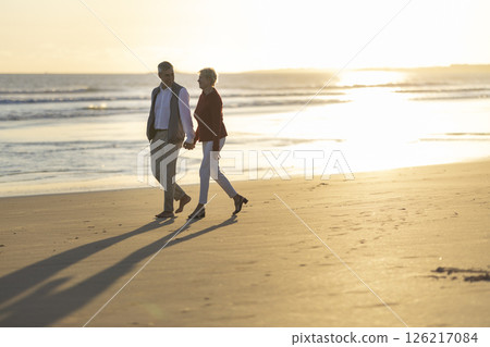 Senior couple walking on the beach at sunset, holding hands 126217084
