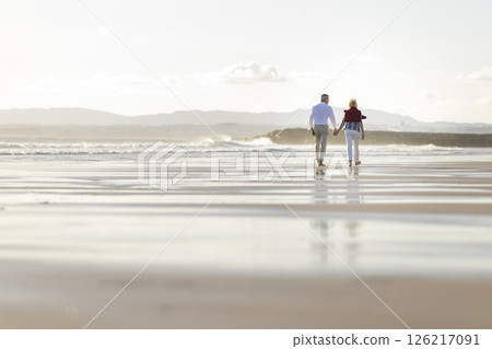 Senior couple walking on beach at sunset holding hands Senior couple walking on beach at sunset holding hands 126217091