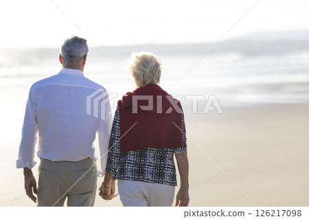 Elderly couple holding hands walking on the beach at sunset 126217098