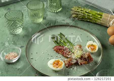 Green asparagus with fried bacon, boiled eggs and parmesan cheese laying on a plate Green asparagus with fried bacon, boiled eggs and parmesan cheese laying on a plate 126217201