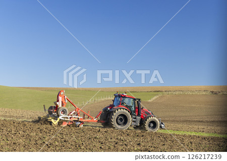 Farmer plowing field in Slovakia with red tractor and cultivator under blue sky 126217239