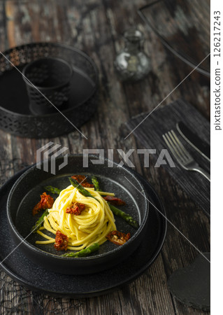 Delicious spaghetti with asparagus and dried tomatoes served on black plate 126217243