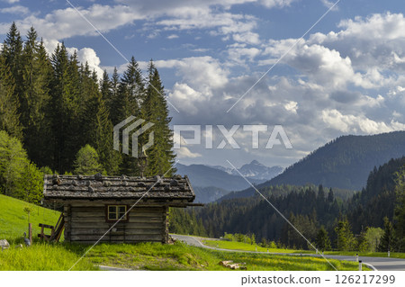 Old wooden hut standing on green meadow in idyllic mountain landscape Old wooden hut standing on green meadow in idyllic mountain landscape 126217299
