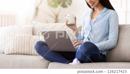 Domestic Relax. Young asian woman resting with laptop and coffee at home, sitting on couch in modern living room, free space Domestic Relax. Young asian woman resting with laptop and coffee at home, sitting on couch in modern living room, free space 126217425