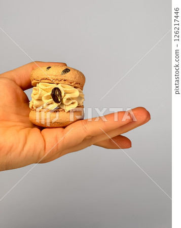 Macaron with coffee filling in hand on gray background 126217446