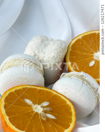 Delicate macarons and orange slices on light drapery 126217471