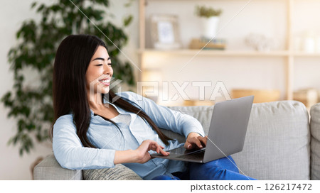 Favorite Pastime. Cheerful Asian Woman Relaxing With Laptop On Couch, Browsing Internet Or Watching Movies, Enjoying Weekend At Home Favorite Pastime. Cheerful Asian Woman Relaxing With Laptop On Couch, Browsing Internet Or Watching Movies, Enjoying Weekend At Home 126217472