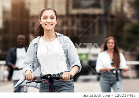 A group of diverse teenagers rides scooters on a busy city street, enjoying the outdoor atmosphere. Their smiles reflect excitement and freedom while they navigate the urban landscape. 126217482