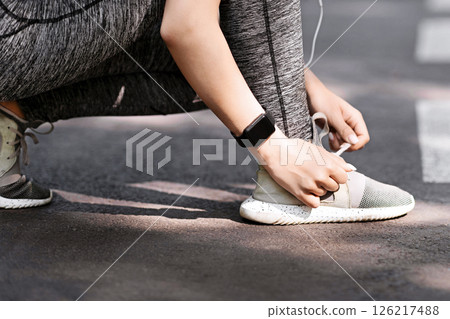 Sporty girl tying shoes laces before running, getting ready for jogging outdoors in park, cropped image with copy space, side view 126217488