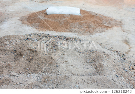 There is construction sand on the ground, and on top of it there is a bag of cement for preparing mortar for laying bricks. 126218243