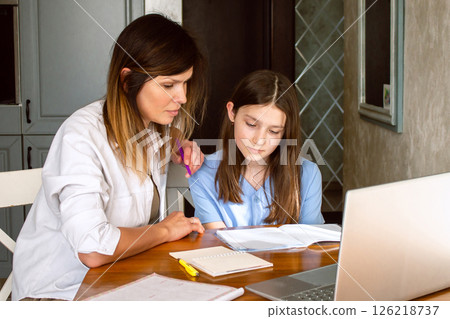 Happy mother with preteen daughter using laptop in home kitchen. Working on school project. Helping with homework using technologies. Happy mother with preteen daughter using laptop in home kitchen. Working on school project. Helping with homework using technologies. 126218737