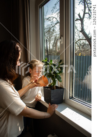 Mother teaches her preschool kid how to water houseplants. Kid involved in family household activity. Early childhood development. 126218741