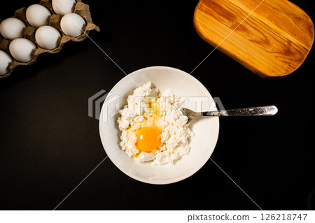 Process of making syrniki. Adding egg to cottage cheese. Top view on black surface. Russian cuisine. Process of making syrniki. Adding egg to cottage cheese. Top view on black surface. Russian cuisine. 126218747