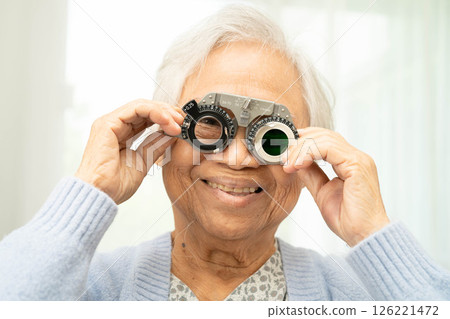 Asian senior woman wearing ophthalmic vision eye test and using optical trial frame. 126221472
