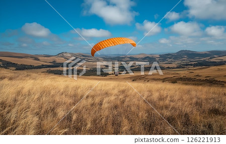 Paraglider soars above golden fields beneath a sky of fluffy clouds 126221913