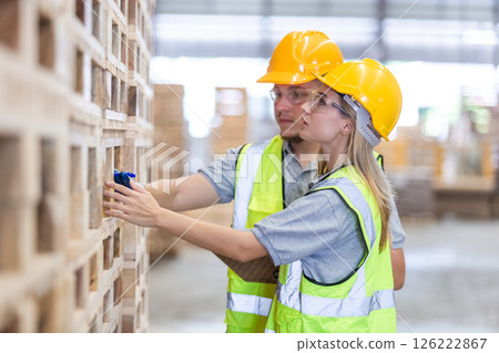 Workers carpenter wearing safety uniform and yellow hard hat working holding clipboard checking quality of wooden products at workshop manufacturing. man and woman worker wood warehouse industry. 126222867