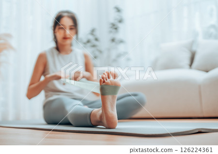 Young Asian woman doing pilates workout using elastic strap pulling with arms Young Asian woman doing pilates workout using elastic strap pulling with arms 126224361