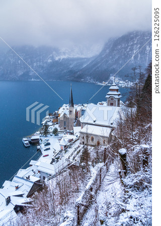 Hallstatt, Austria. Idyllic Alpine village snow-covered, serene lake, majestic mountains  shrouded in a winter blizzard. 126225095