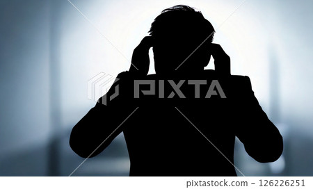Silhouette of a businessman panicking with both hands on his head_Dark facility background 126226251