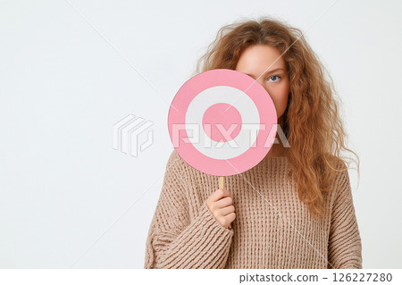 A woman in a light sweater holds a target with arrows against light background. Victim, targeted advertising, bullying, abuse, harassment, stress, fear 126227280