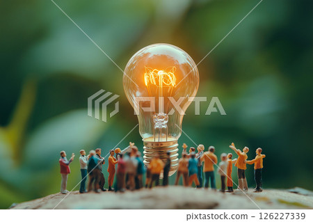 A group of small figurines surrounds a glowing light bulb on green grass, evoking themes of innovation, teamwork, and sustainability in a creative and conceptual composition. Ideas and unity concept A group of small figurines surrounds a glowing light bulb on green grass, evoking themes of innovation, teamwork, and sustainability in a creative and conceptual composition. Ideas and unity concept 126227339