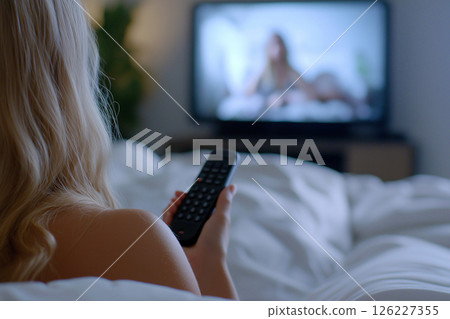 Close-up of a hand holding a remote with a blurry romantic scene on TV. Watching movies, porn, tv-series. A person holds a remote control, focusing on a romantic movie scene in a cozy setting. 126227355