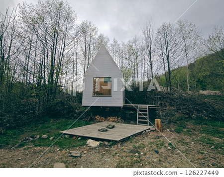The white wooden board hut with big window between trees, 126227449