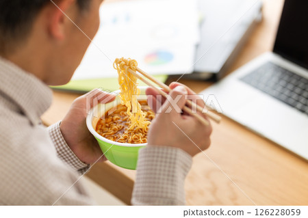 一位中年男子在辦公室工作時吃杯拉麵 126228059