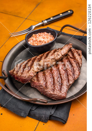 Grilled Denver steak, perfectly seared with beautiful grill marks, showcasing its juicy tenderness and rich flavor. orange background. top view 126228184